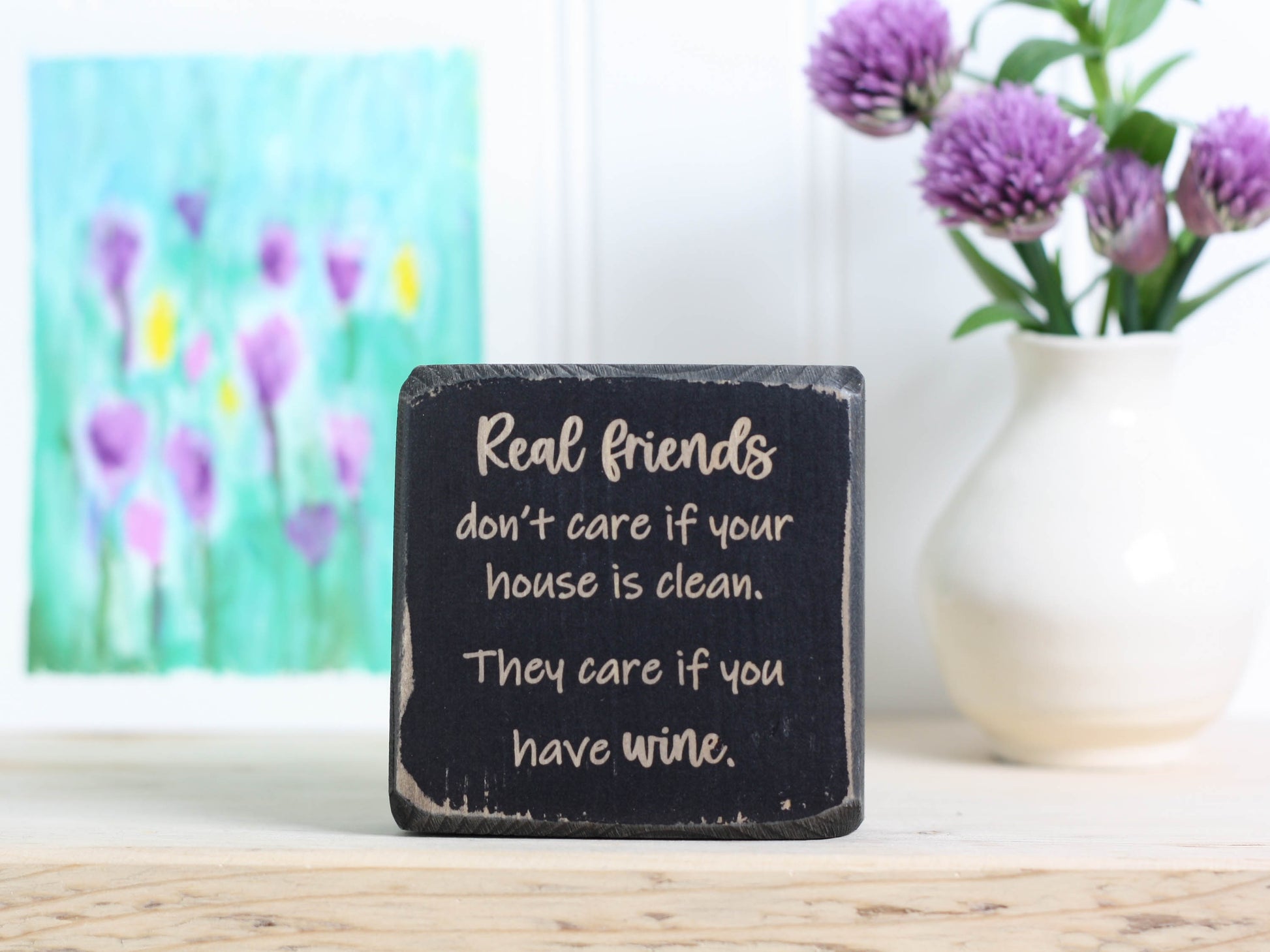 Small wood sign in distressed black with the saying "Real friends don't care if your house is clean. They care if you have wine."