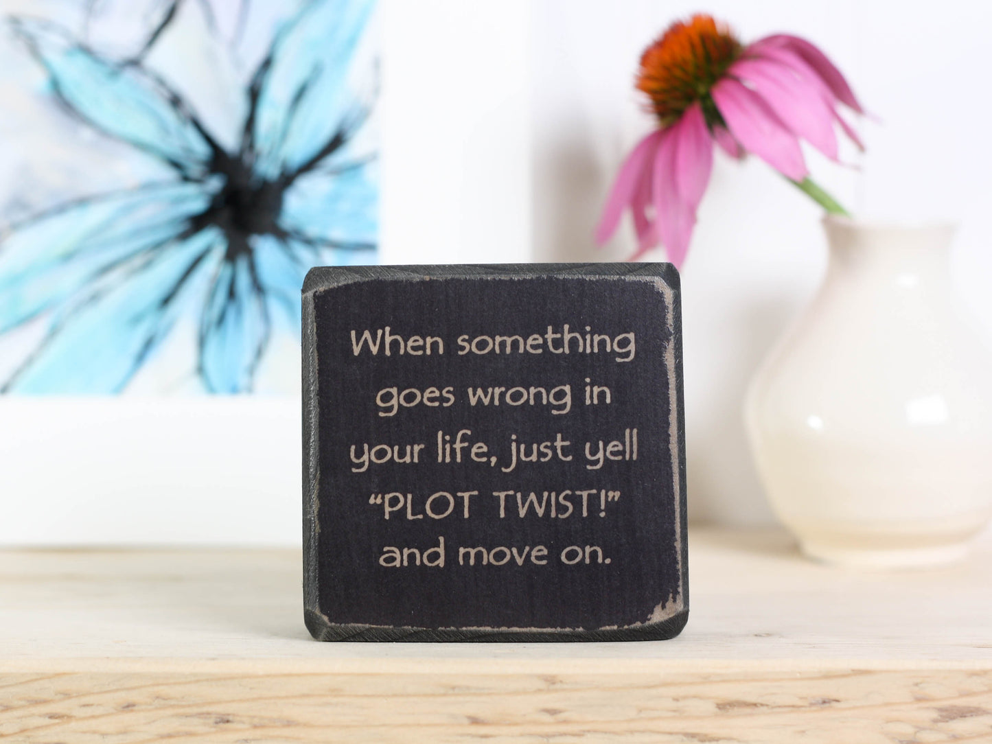Small motivational wood sign in distressed black with the saying "when something goes wrong in your life, just yell "PLOT TWIST" and move one.