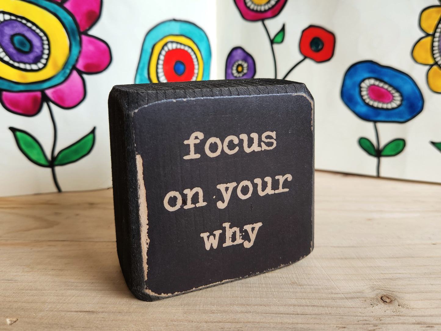 Black block sign with 'focus on your why' text against a colorful floral background
