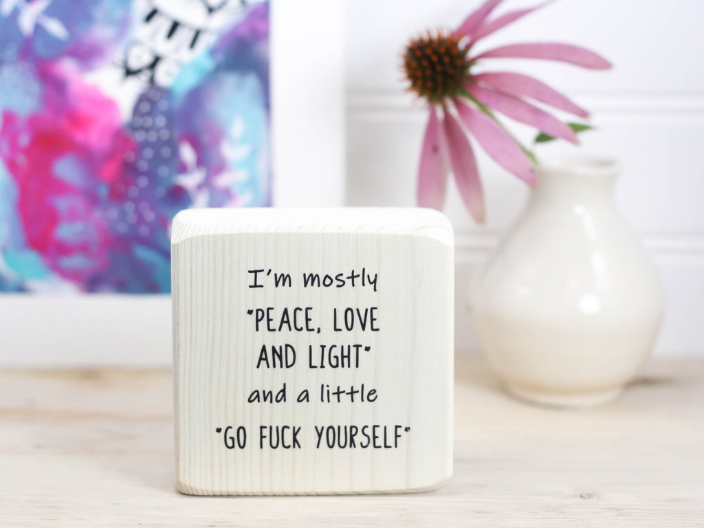 Small funny wood sign in whitewash with the saying "I'm mostly peace, love and light and a little go fuck yourself".