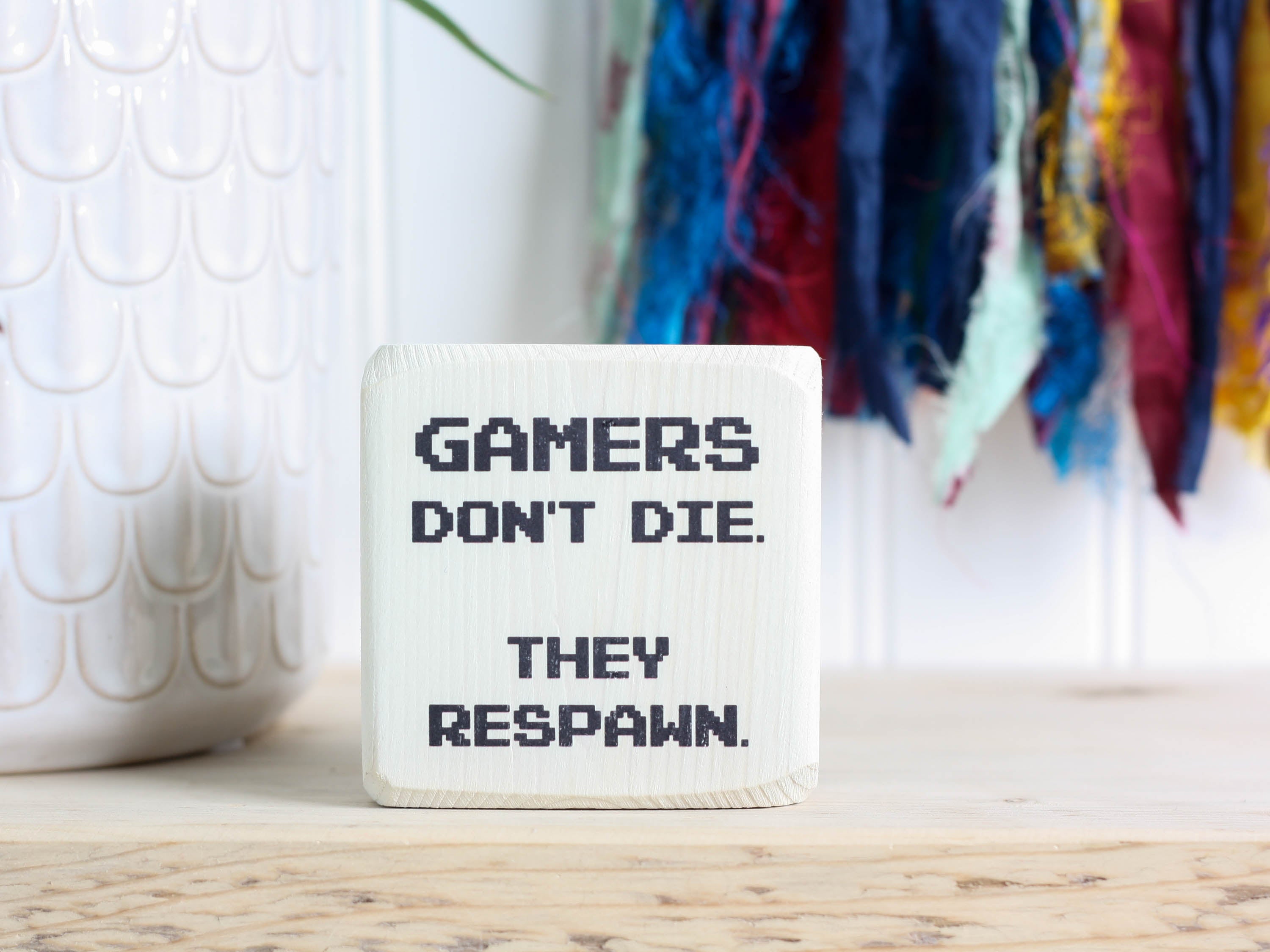 Small wood sign in whitewash with the saying "Gamers don't die. They respawn."