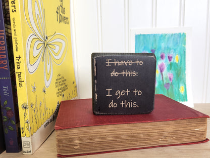Small black block sign with motivational quote on a stack of books with colorful covers.