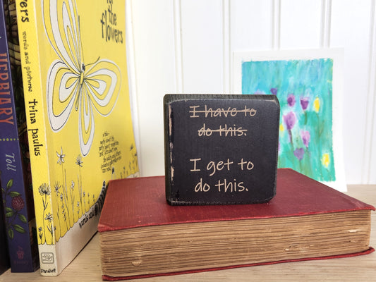Small black block sign with motivational quote on a stack of books with colorful covers.