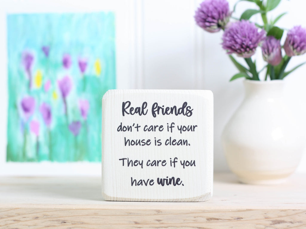 Small wood sign in whitewash with the saying "Real friends don't care if your house is clean. They care if you have wine."