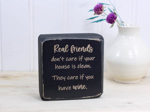 Small wood sign in distressed black with the saying "Real friends don't care if your house is clean. They care if you have wine."