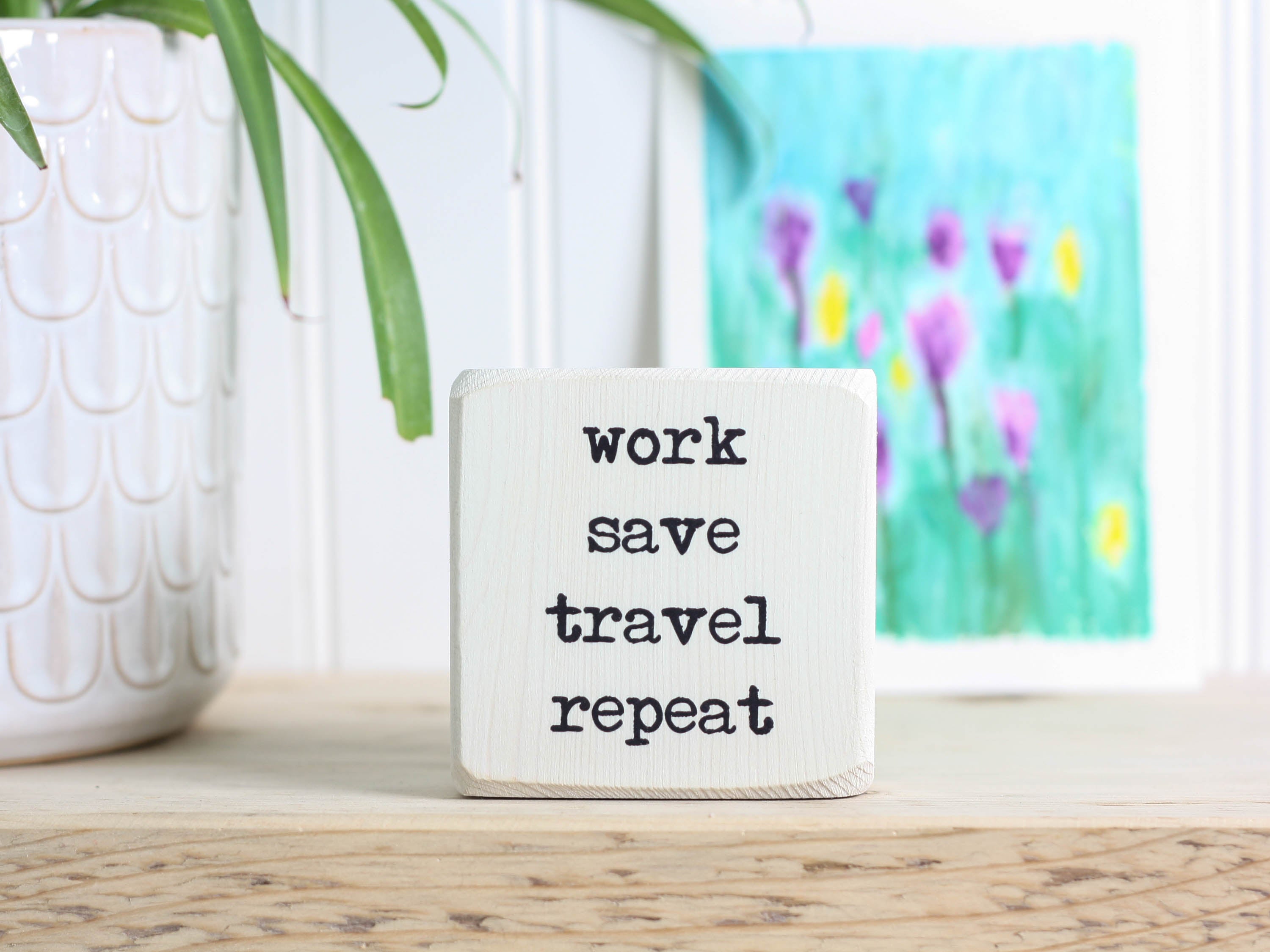 Small wood travel sign in whitewash with the saying "work save travel repeat"