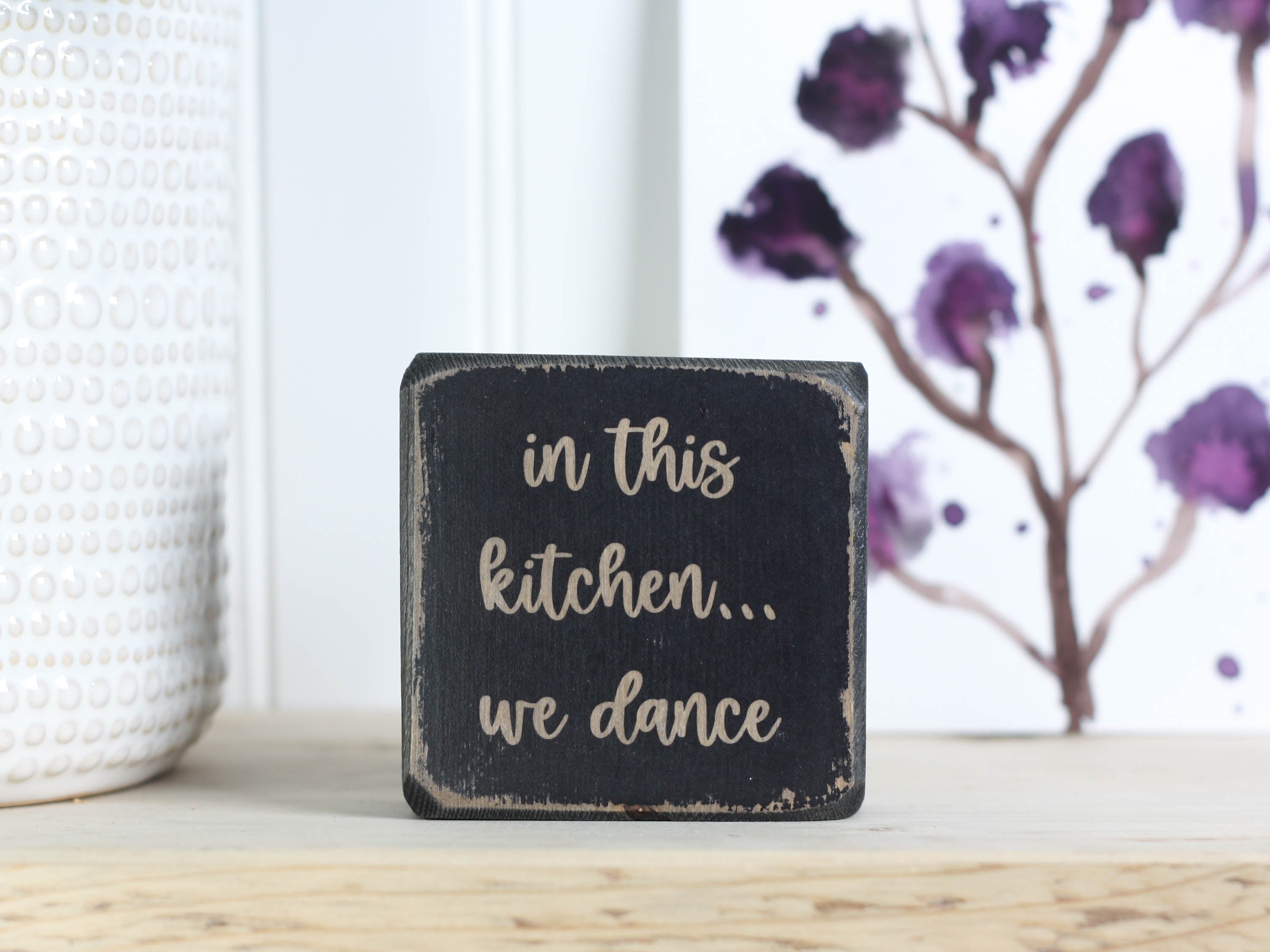 Small wooden decor in distressed black with the saying "in this kitchen... we dance"
