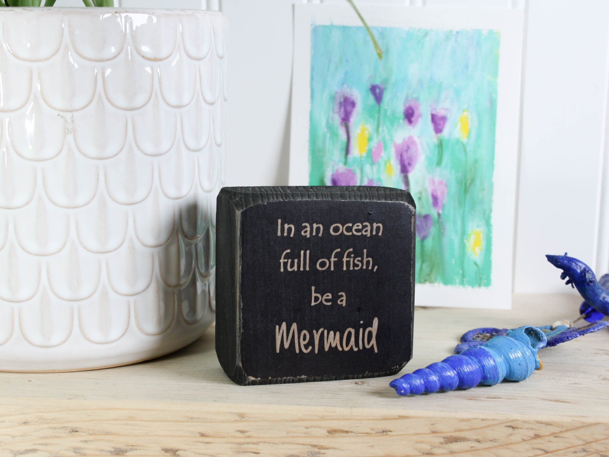 Small distressed black wood sign with the text "in an ocean full of fish, be a mermaid"