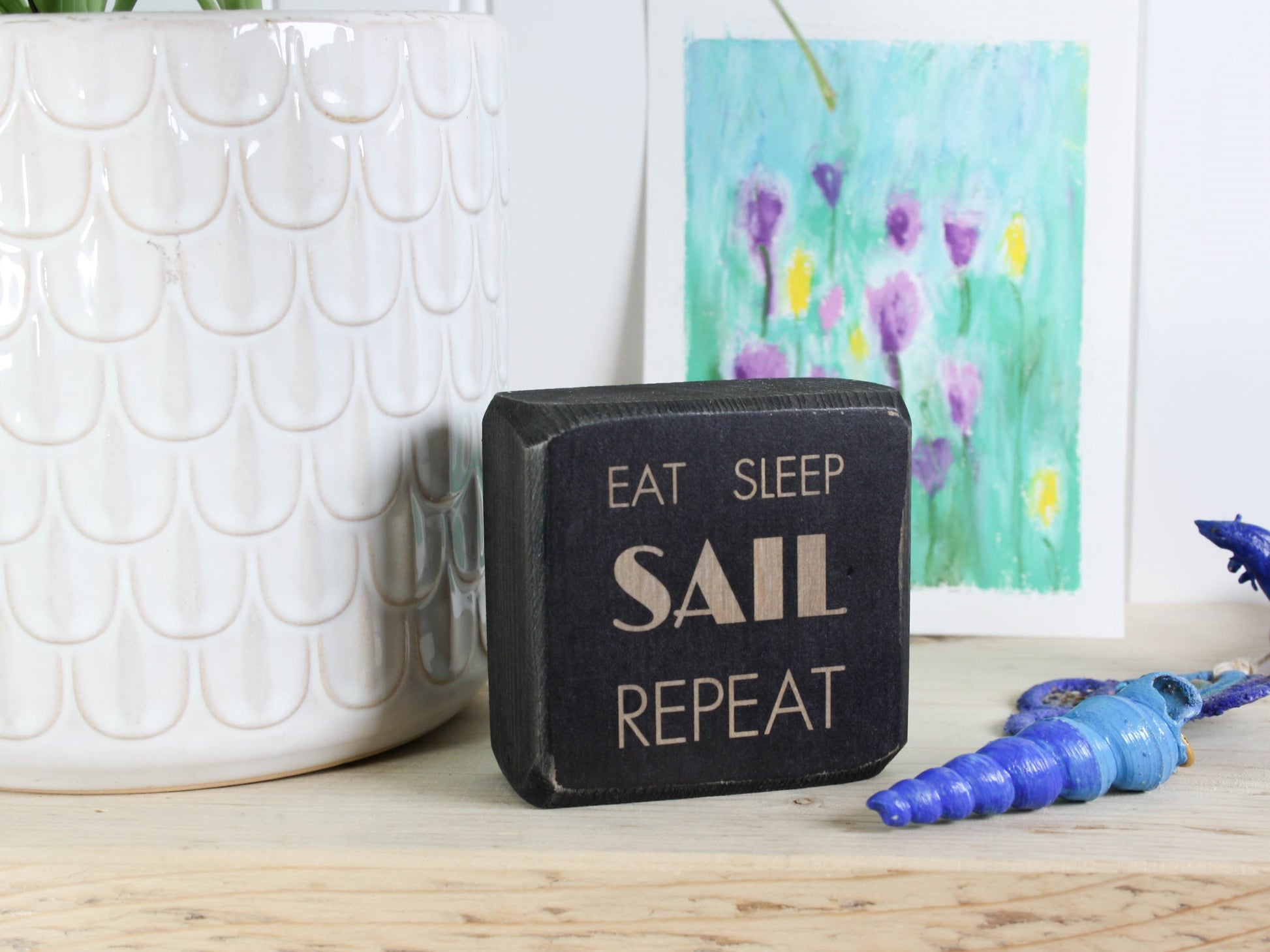 Small distressed black wood sign with the text "eat sleep sail repeat"