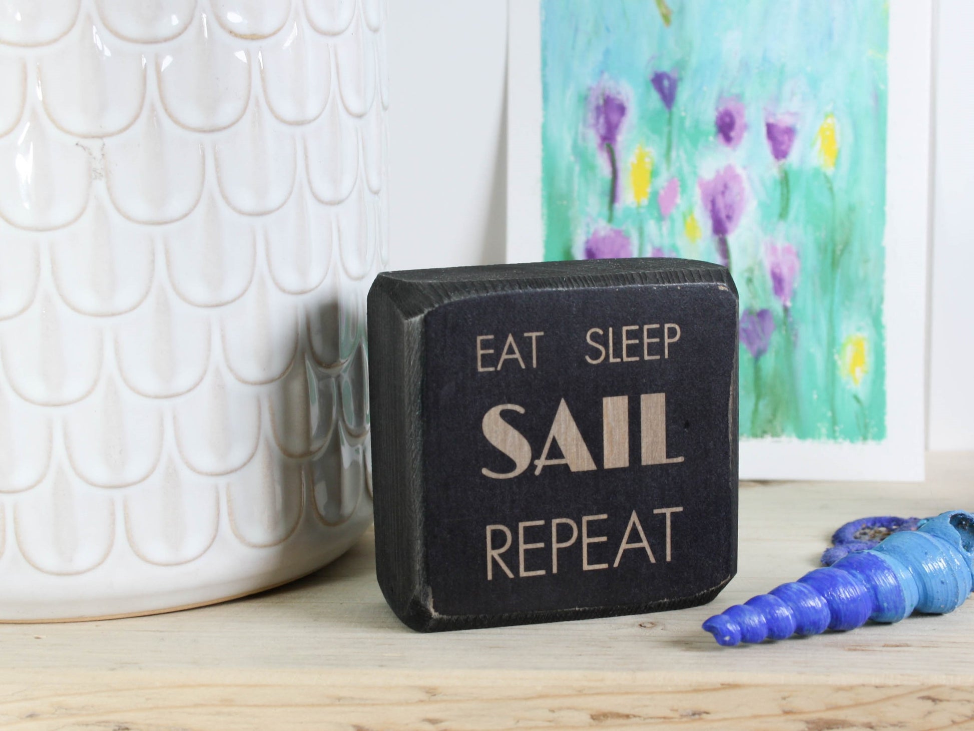 Small distressed black wood sign with the text "eat sleep sail repeat"