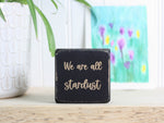 Small wood sign in distressed black with the saying "We are all stardust"