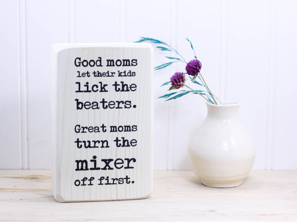 Small funny wood kitchen sign in whitewash with the saying "Good moms let their kids lick the beaters. Great moms turn the mixer off first."