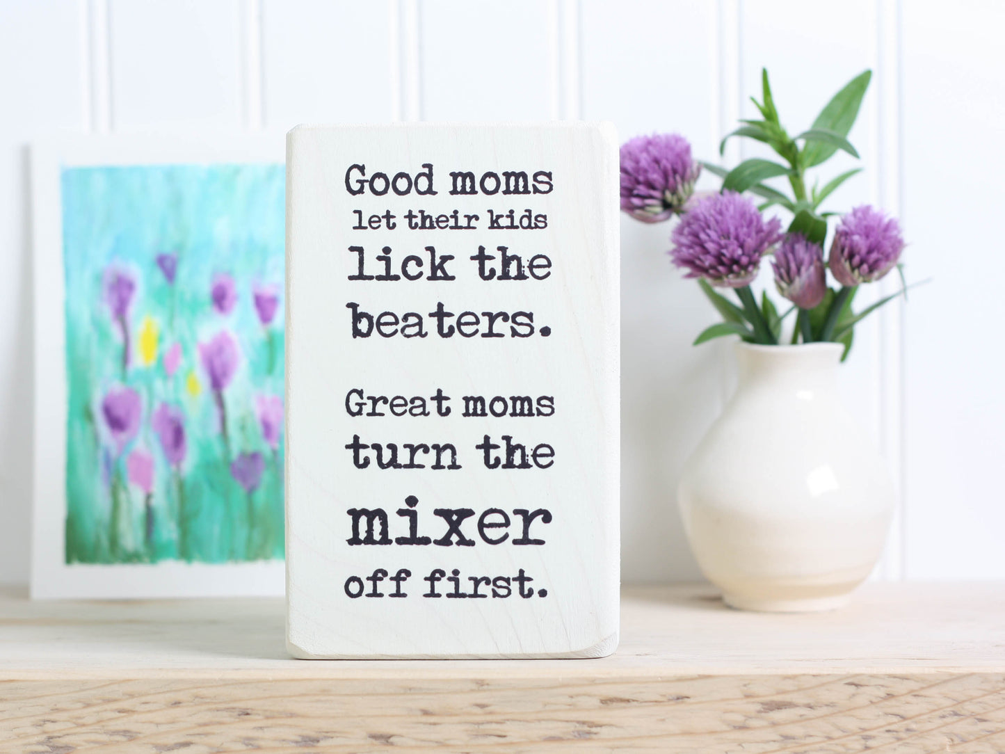 Small funny wood kitchen sign in whitewash with the saying "Good moms let their kids lick the beaters. Great moms turn the mixer off first."