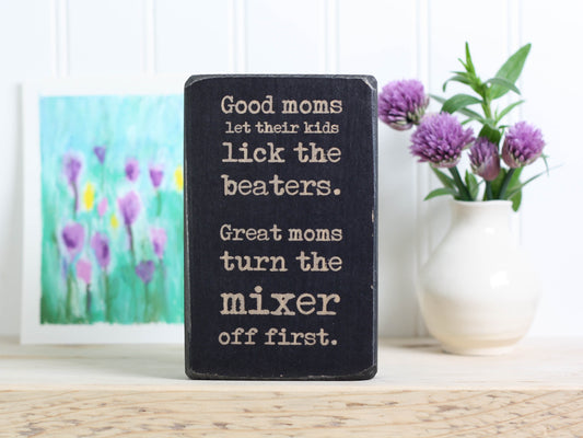 Small funny wood kitchen sign in distressed black with the saying "Good moms let their kids lick the beaters. Great moms turn the mixer off first."