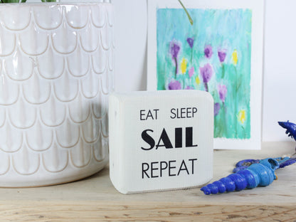 Small whitewashed wood sign with the text "eat sleep sail repeat"