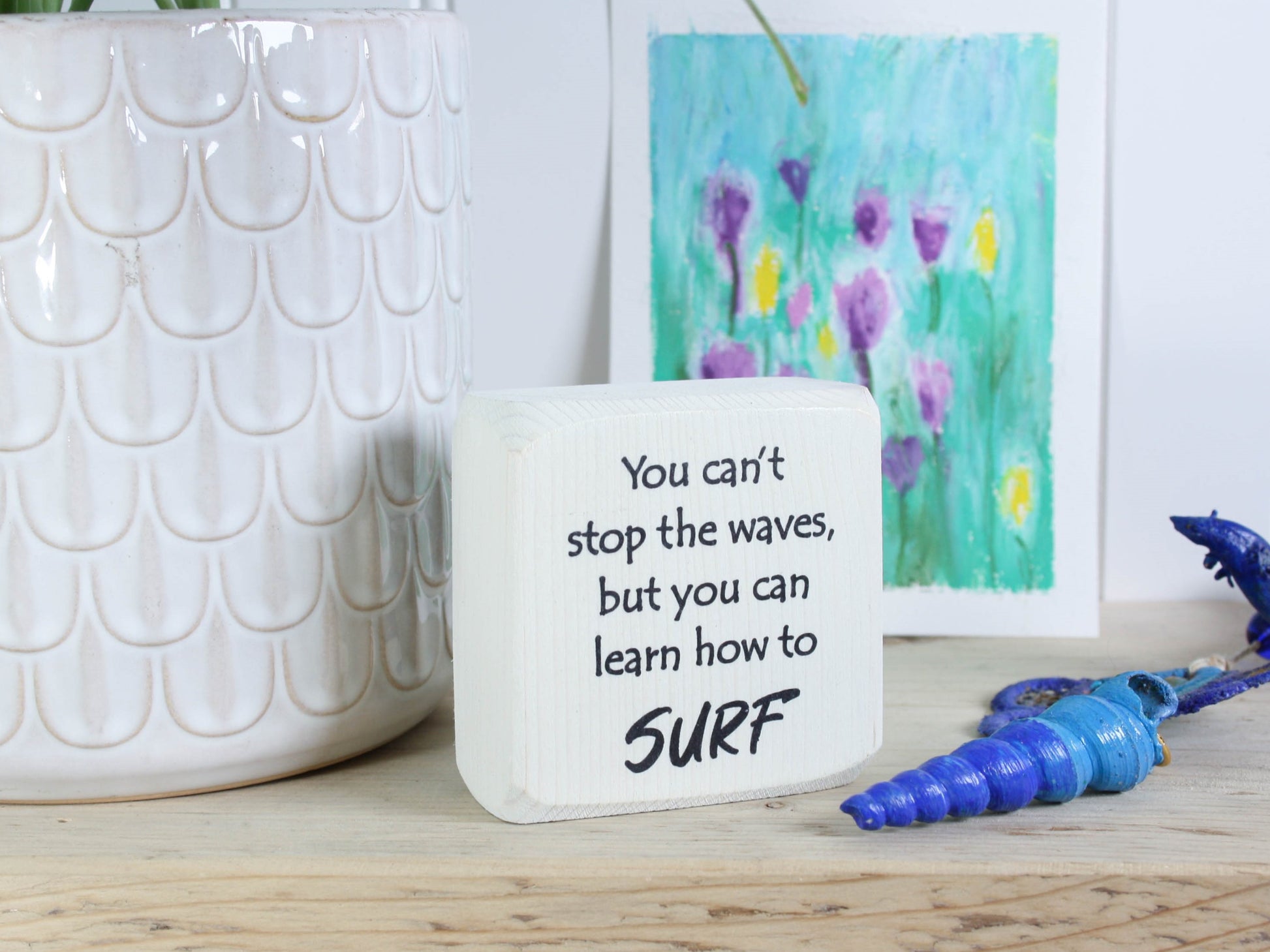Small whitewashed wood sign with the saying "You can't stop the waves, but you can learn to surf"
