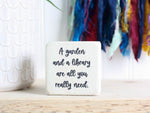 Small wood sign in whitewash with the saying "A garden and a library are all you really need."