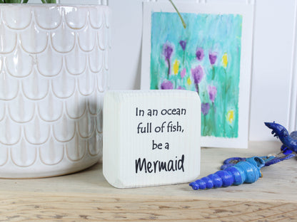Small distressed black wood sign with the text "in an ocean full of fish, be a mermaid"