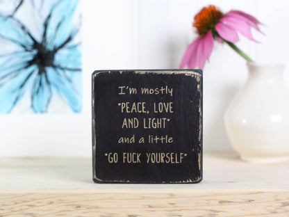 Small funny wood sign in distressed black with the saying "I'm mostly peace, love and light and a little go fuck yourself".