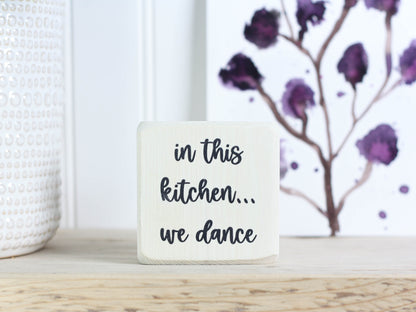 Small wooden decor in whitewash with the saying "in this kitchen... we dance"