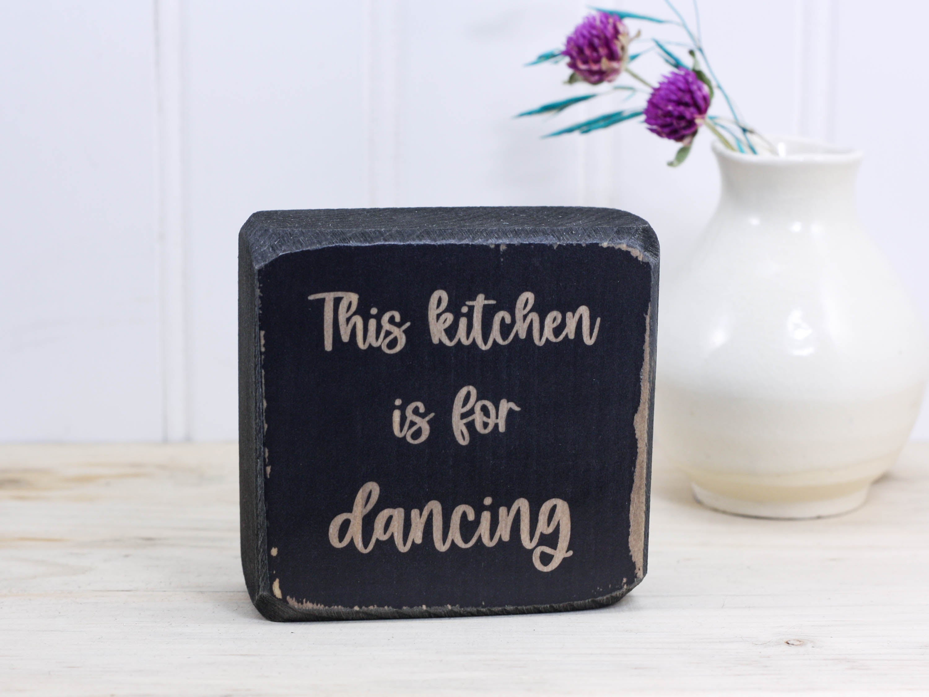 Small wooden decor in distressed black with the saying "This kitchen is for dancing".
