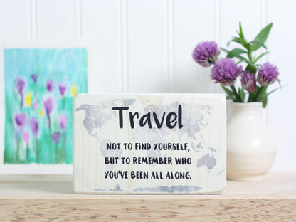 Small wood travel sign in whitewash with the saying "Travel not to find yourself, but to remember who you've been all along."