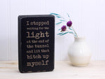 Small wood quote block in distressed black with the saying "I stopped waiting for the light at the end of the tunnel and lit that bitch up myself."