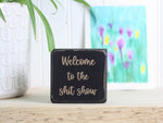 Small wood shelf sitter in distressed black with the saying "Welcome to the shit show".