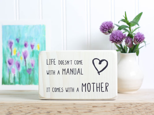 Small wood decor sign in whitewash with the saying "Life doesn't come with a manual. It comes with a mother."