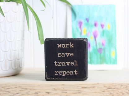 Small wood travel sign in distressed black with the saying "work save travel repeat"