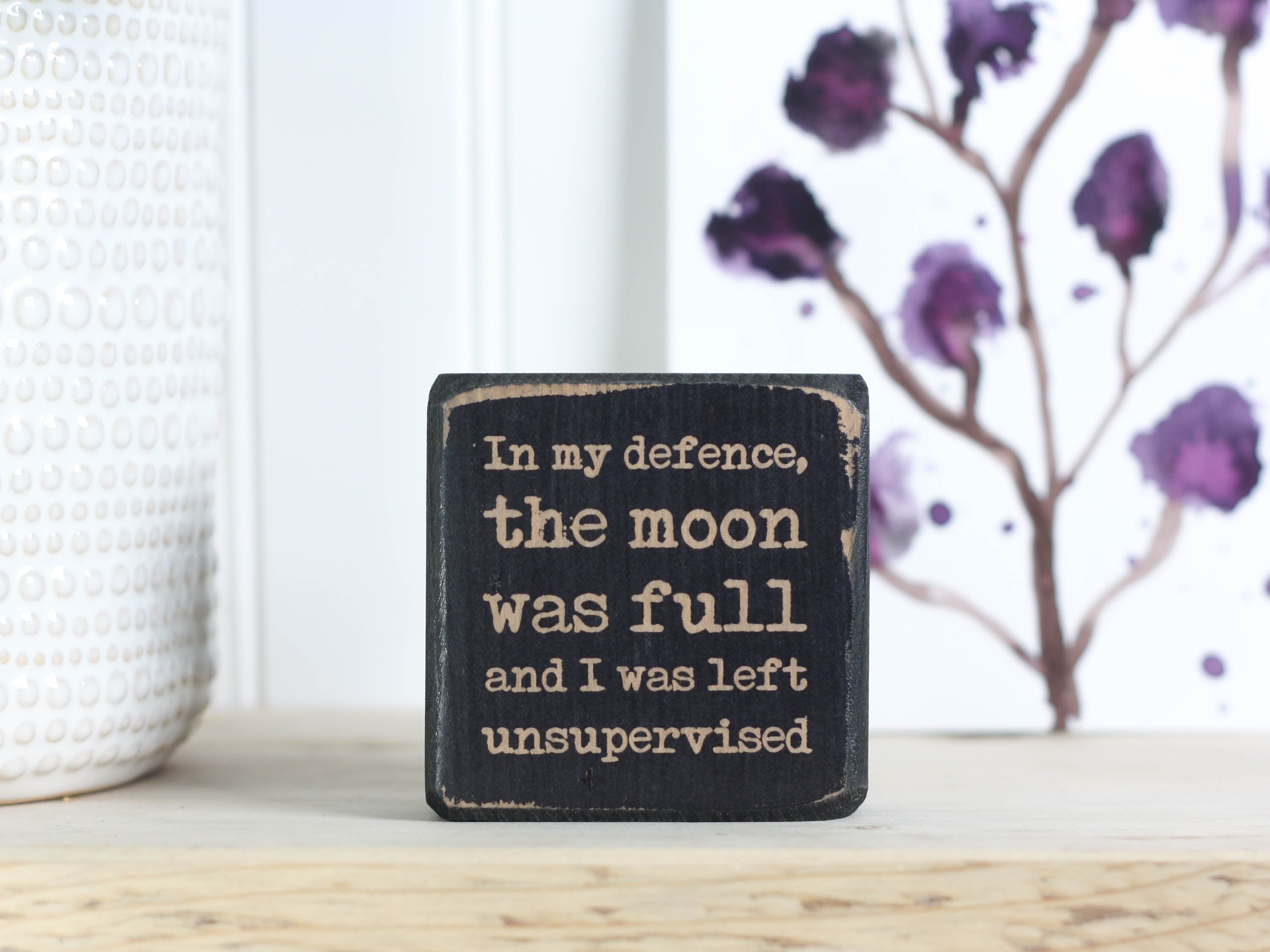 Small wood sign in distressed black with the saying "In my defense, the moon was full and I was left unsupervised."