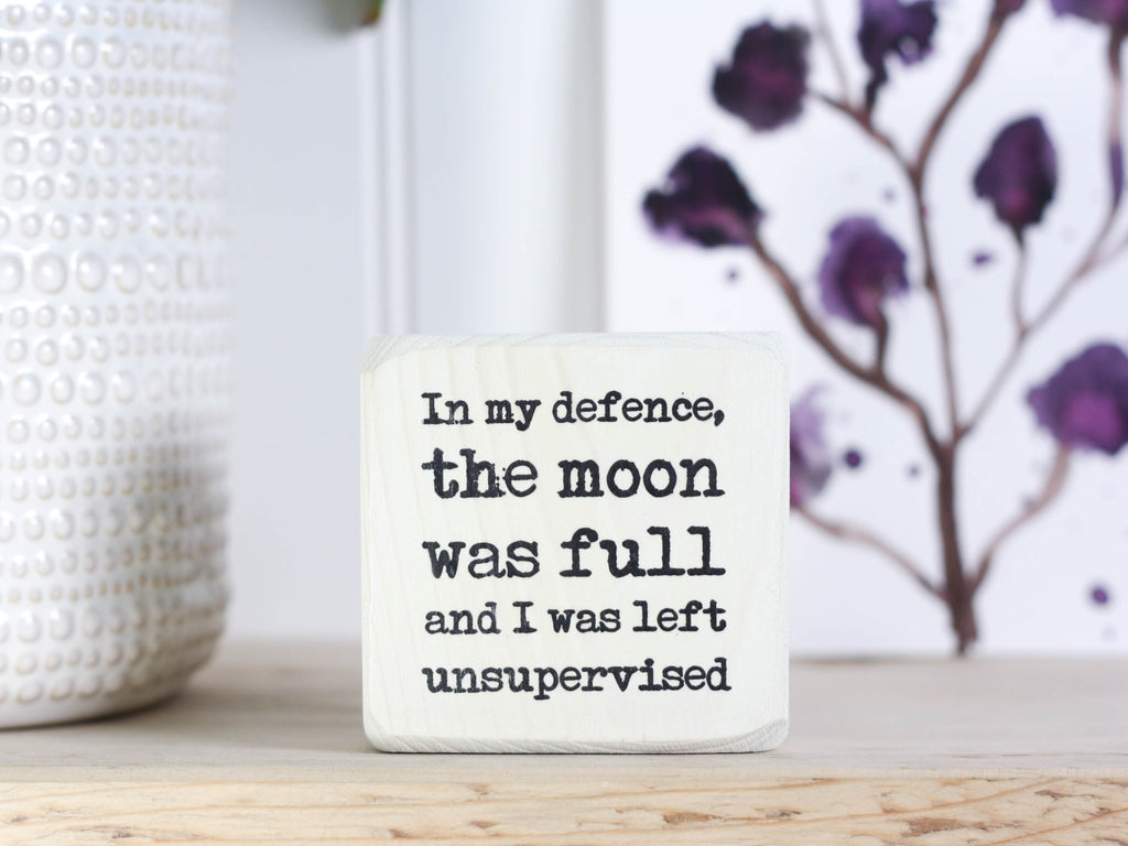 Small wood sign in whitewash with the saying "In my defense, the moon was full and I was left unsupervised."