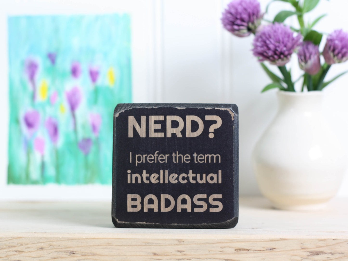 Small desk sign in distressed black with the saying "Nerd? I prefer the term intellectual badass."