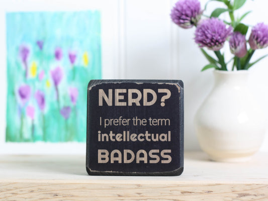 Small desk sign in distressed black with the saying "Nerd? I prefer the term intellectual badass."