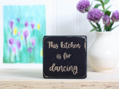 Small wooden decor in distressed black with the saying "This kitchen is for dancing".