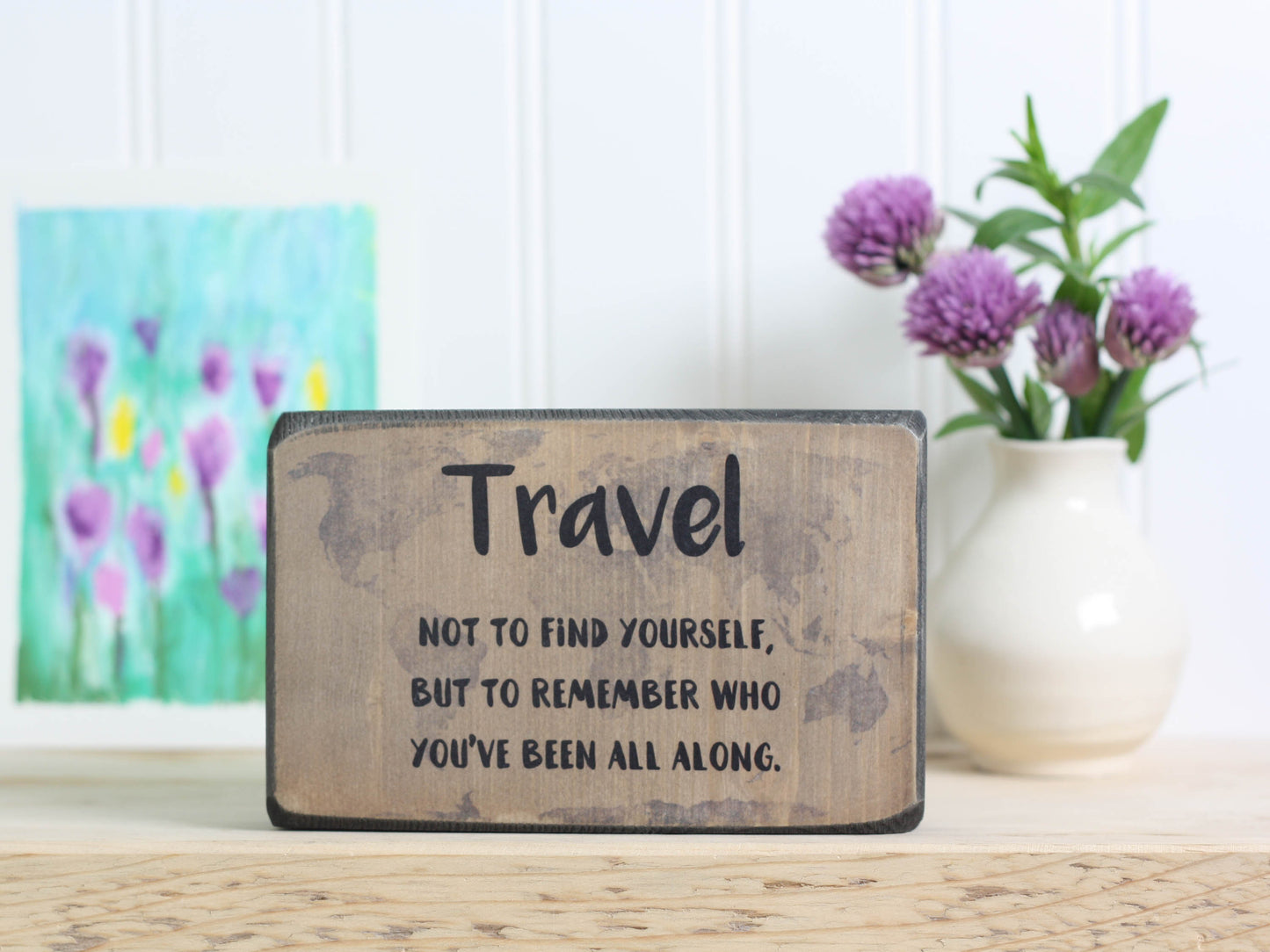 Small wood travel sign in distressed black with the saying "Travel not to find yourself, but to remember who you've been all along."