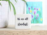 Small wood sign in whitewash with the saying "We are all stardust"