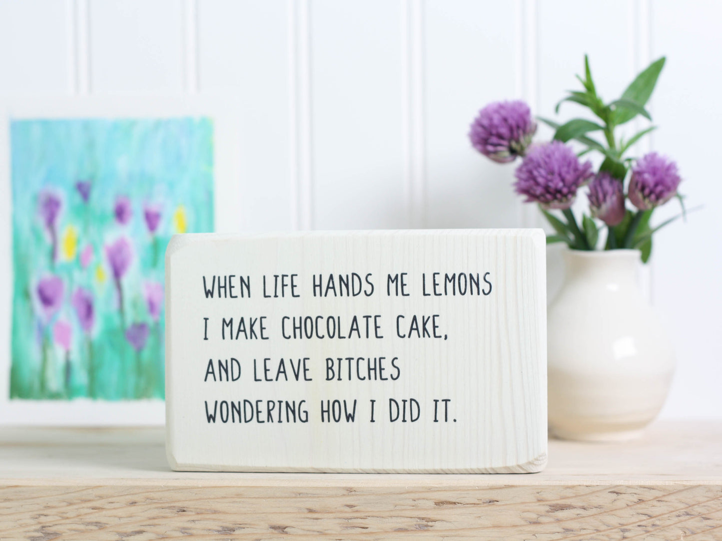 Small free-standing wood sign in whitewash with the saying "When life hands me lemons I make chocolate cake, and leave bitches wondering how I did it.