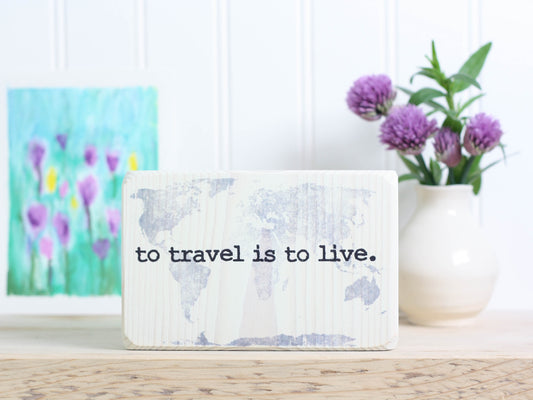 Small wood travel sign in whitewash with the saying "To travel is to live".