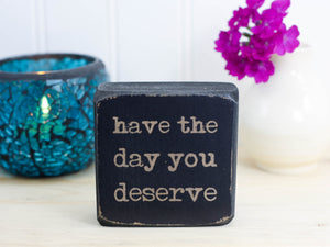 small wood sign in distressed black with the text "have the day you deserve"