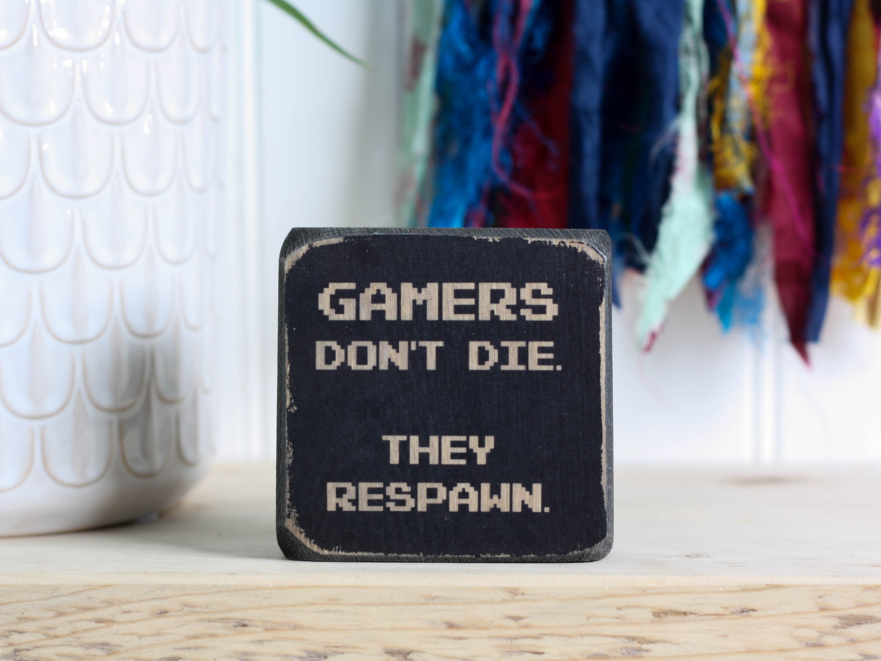 Small wood sign in distressed black with the saying "Gamers don't die. They respawn."