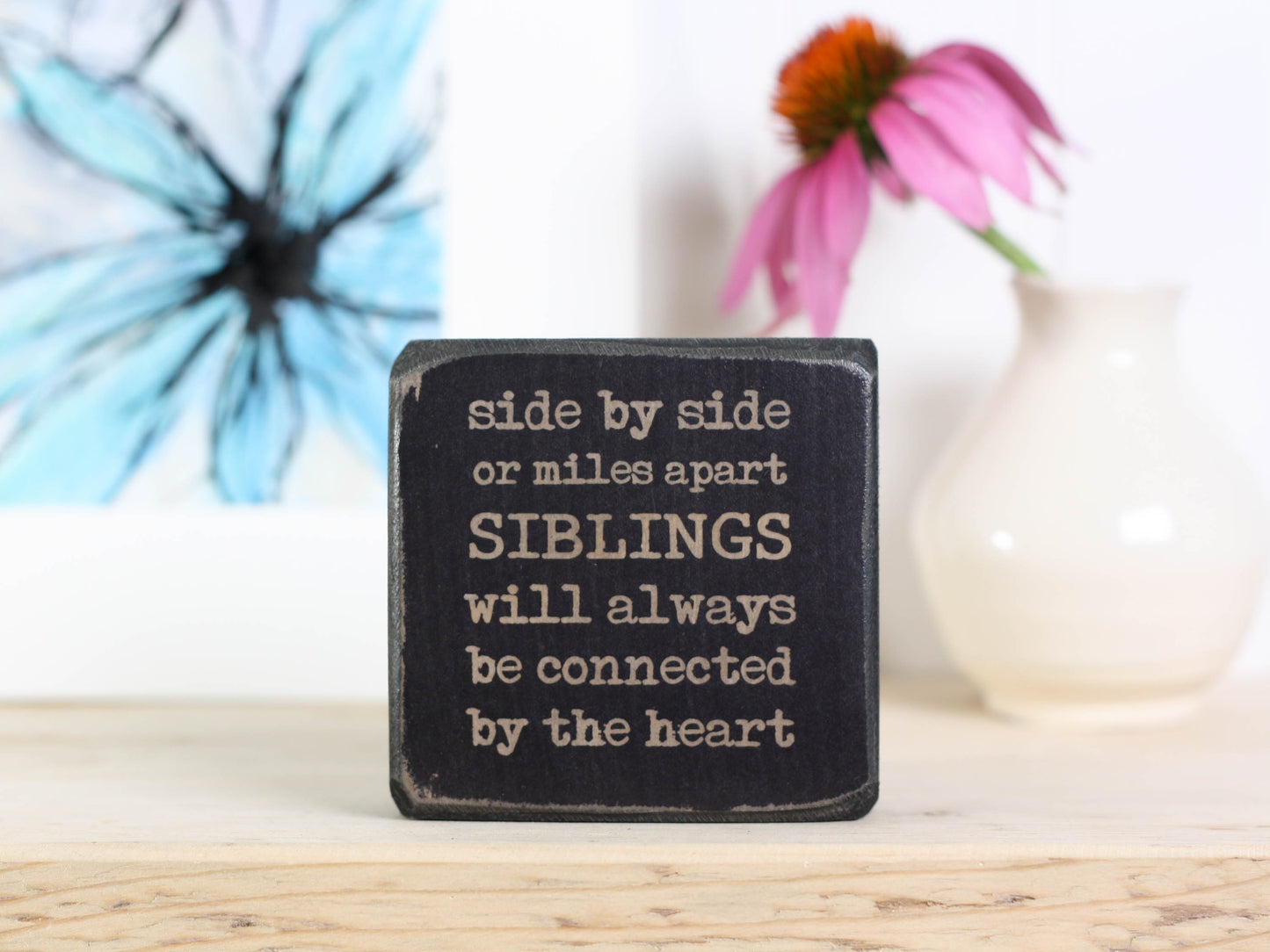 Small wood block with sister quote in distressed black that reads "Side by side or miles apart siblings will always be connected by the heart."