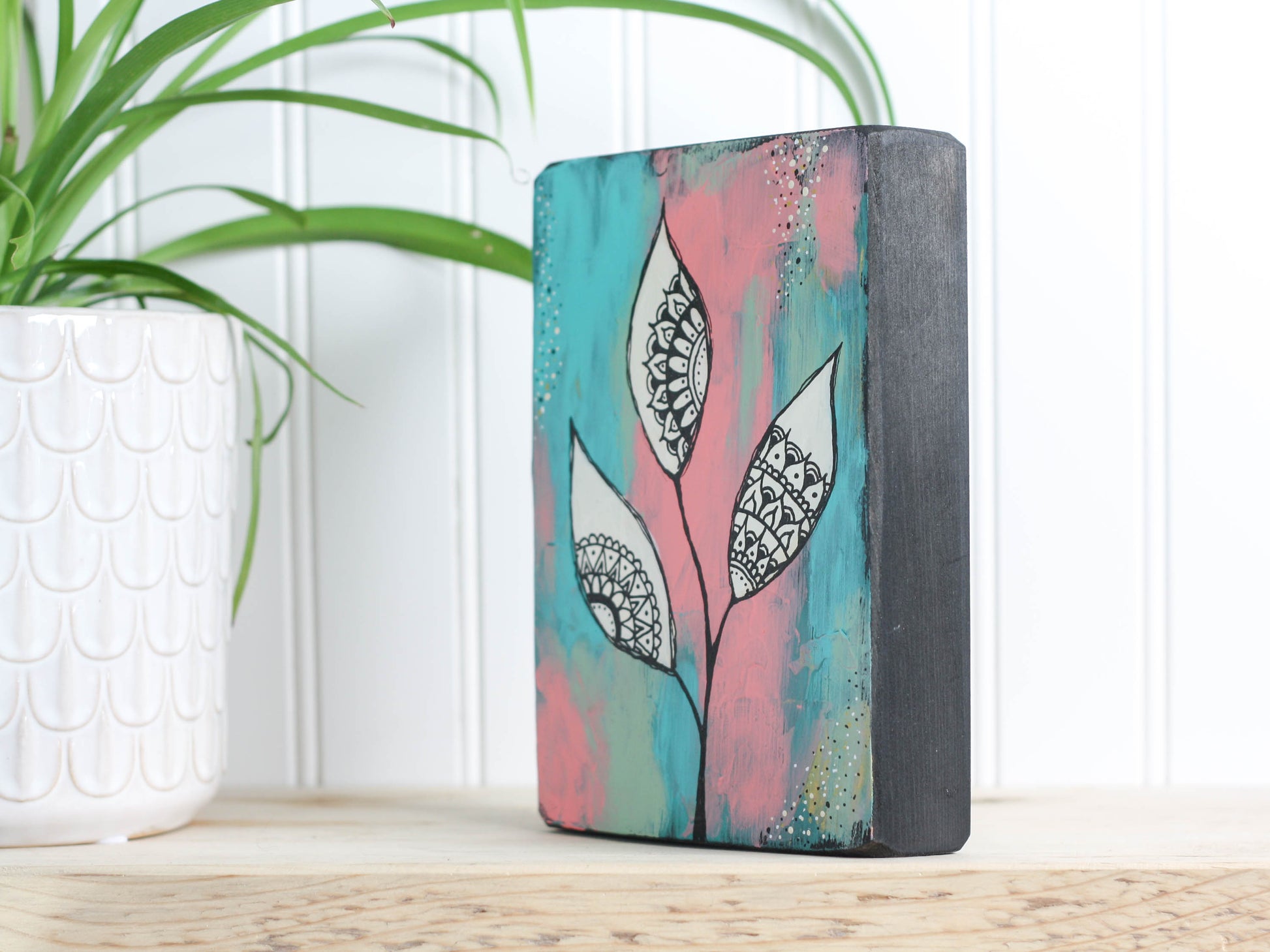 Original mixed media art on a wood block, with a background of teal, peach and dusty light green, with white leaves and mandala inspired shapes inside the leaves.