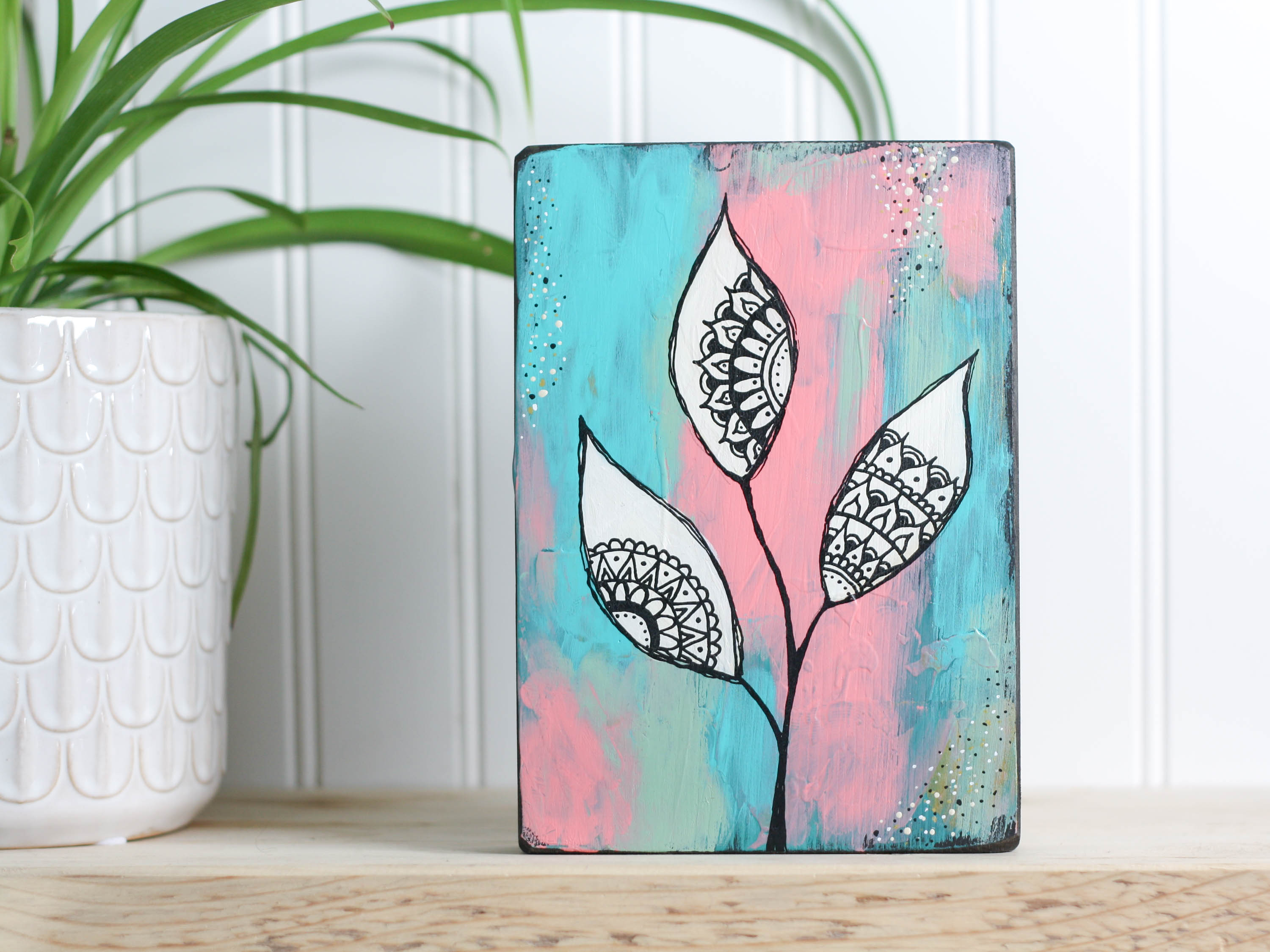 Original mixed media art on a wood block, with a background of teal, peach and dusty light green, with white leaves and mandala inspired shapes inside the leaves.