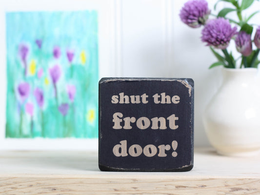 Small, freestanding, distressed black, solid wood sign with funny saying "shut the front door!"