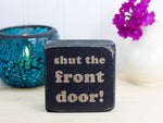 Small, freestanding, distressed black, solid wood sign with funny saying "shut the front door!"