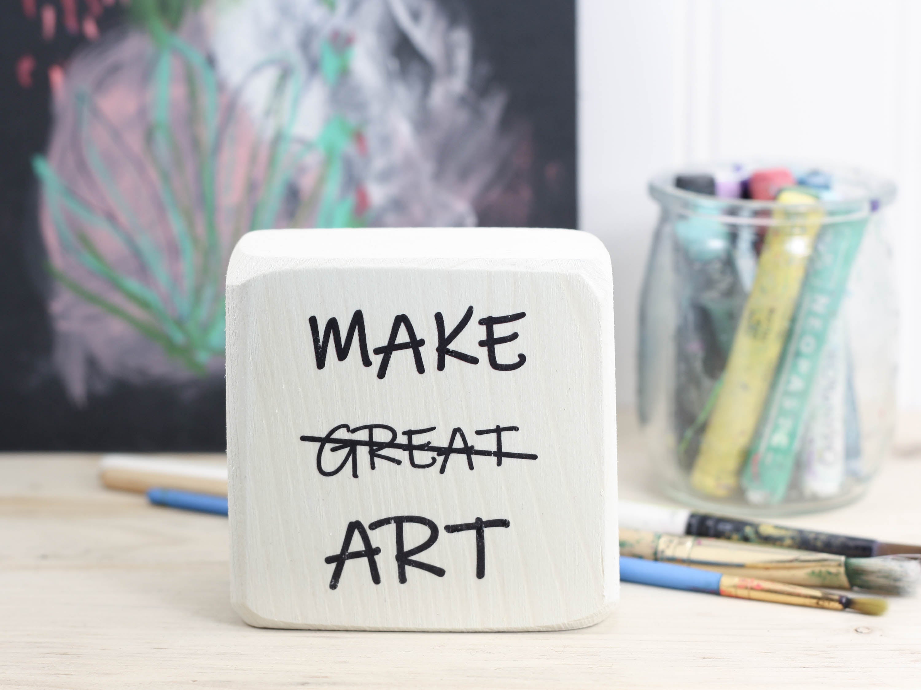 small freestanding sign in whitewash with the text "Make great art" and the word great is crossed out