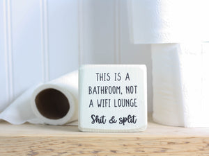 small whitewashed wood bathroom sign with the text "this is a bathroom, not a wifi lounge. Shit & split"