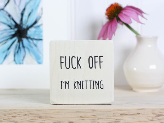 Small whitewashed wood sign with the saying "fuck off I'm knitting"