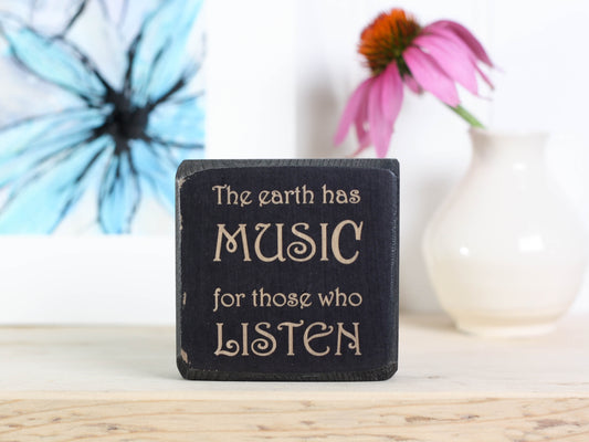 Mini wood sign in distressed black with the saying "the earth has music for those who listen."